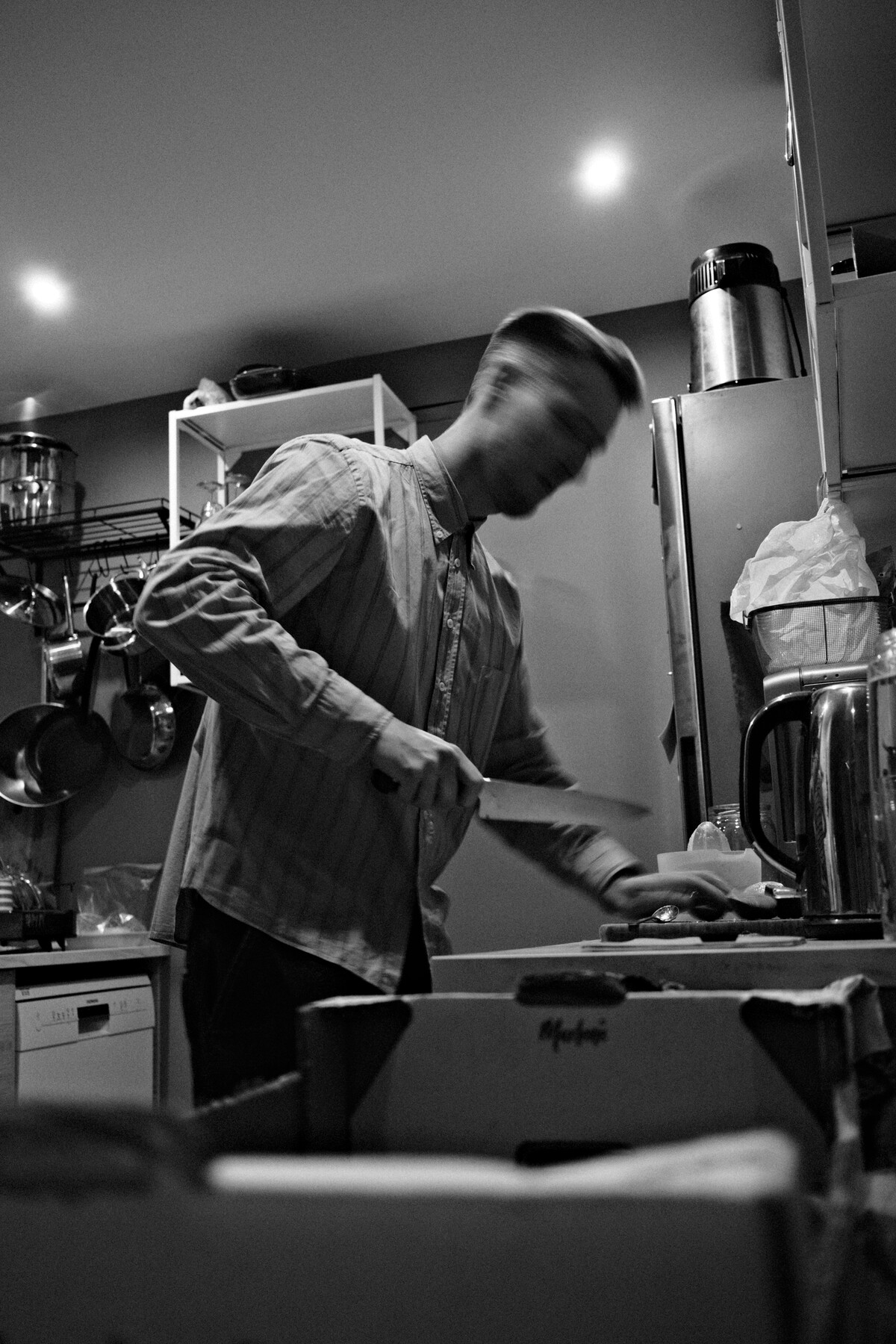 A person in a striped shirt preparing food in a small kitchen, blurred with motion, in black and white.