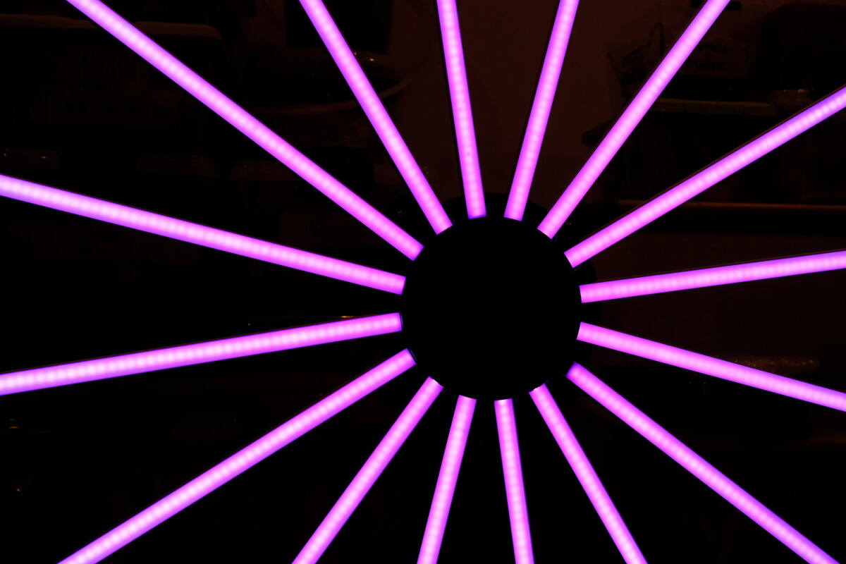 Close-up of a magenta LED starburst installation with fifteen spokes radiating from a dark center against a black background.
