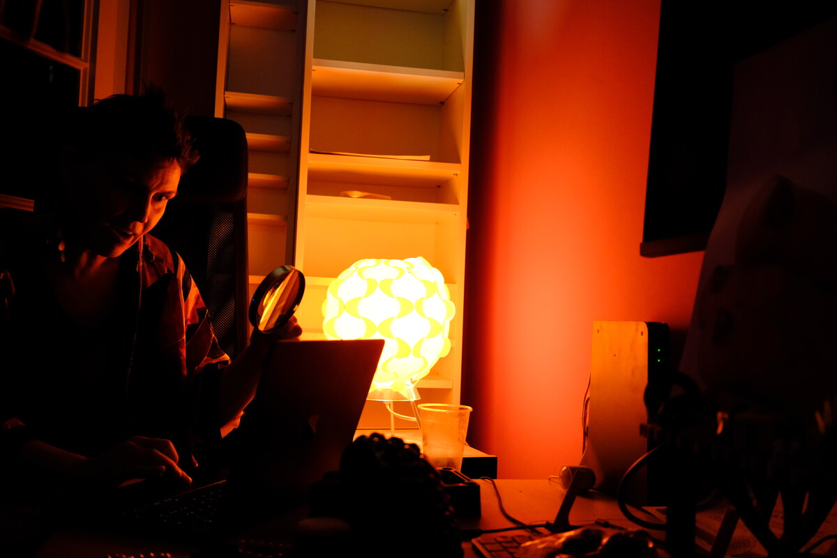 A dimly lit room with a geometric paper globe lamp, a silhouetted figure, and pink-red ambient light casting warm shadows.