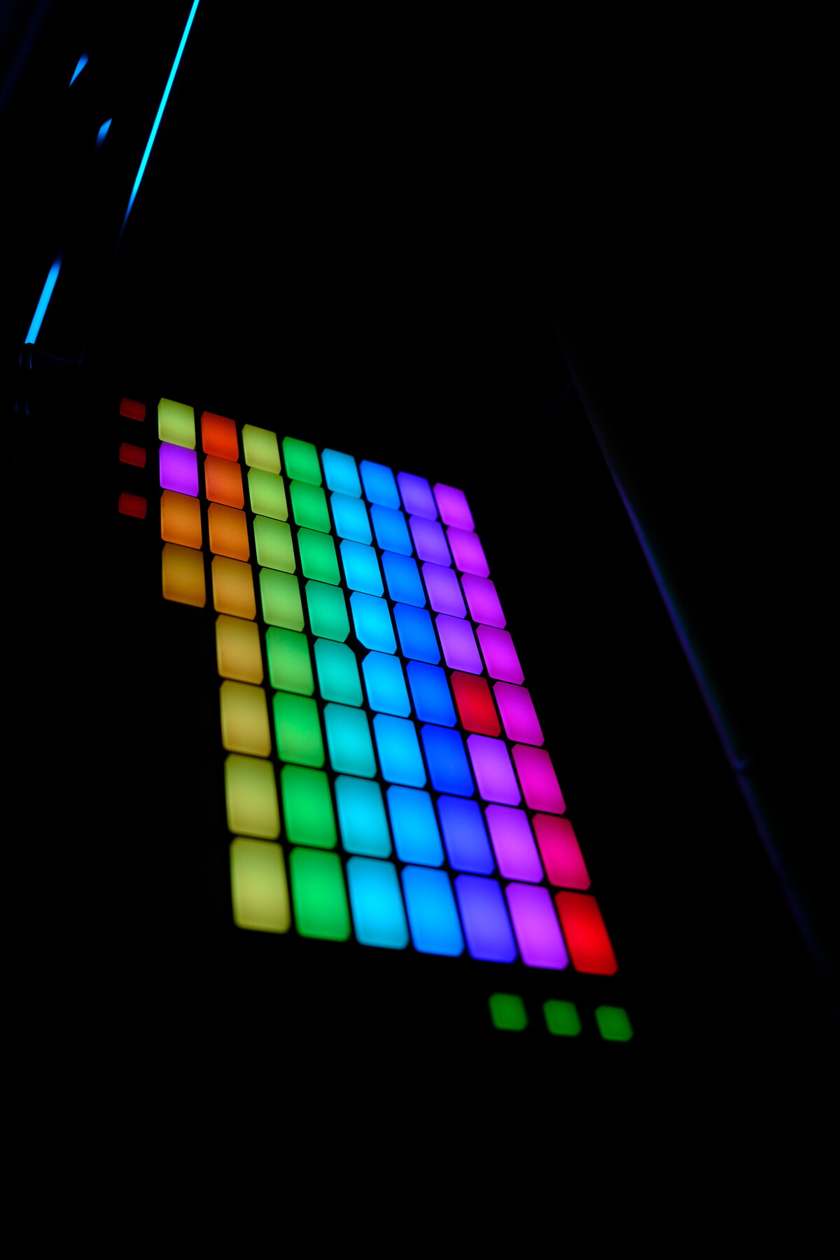 A grid of glowing colored LED squares mounted on a dark wall &mdash; greens, purples, pinks, blues, oranges cycling through a rainbow pattern, with a cyan LED strip above.