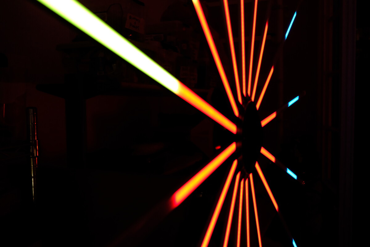 Orange and cyan LED light rays radiating from a central hub against a dark background &mdash; one of Rob&rsquo;s handmade lighting installations.