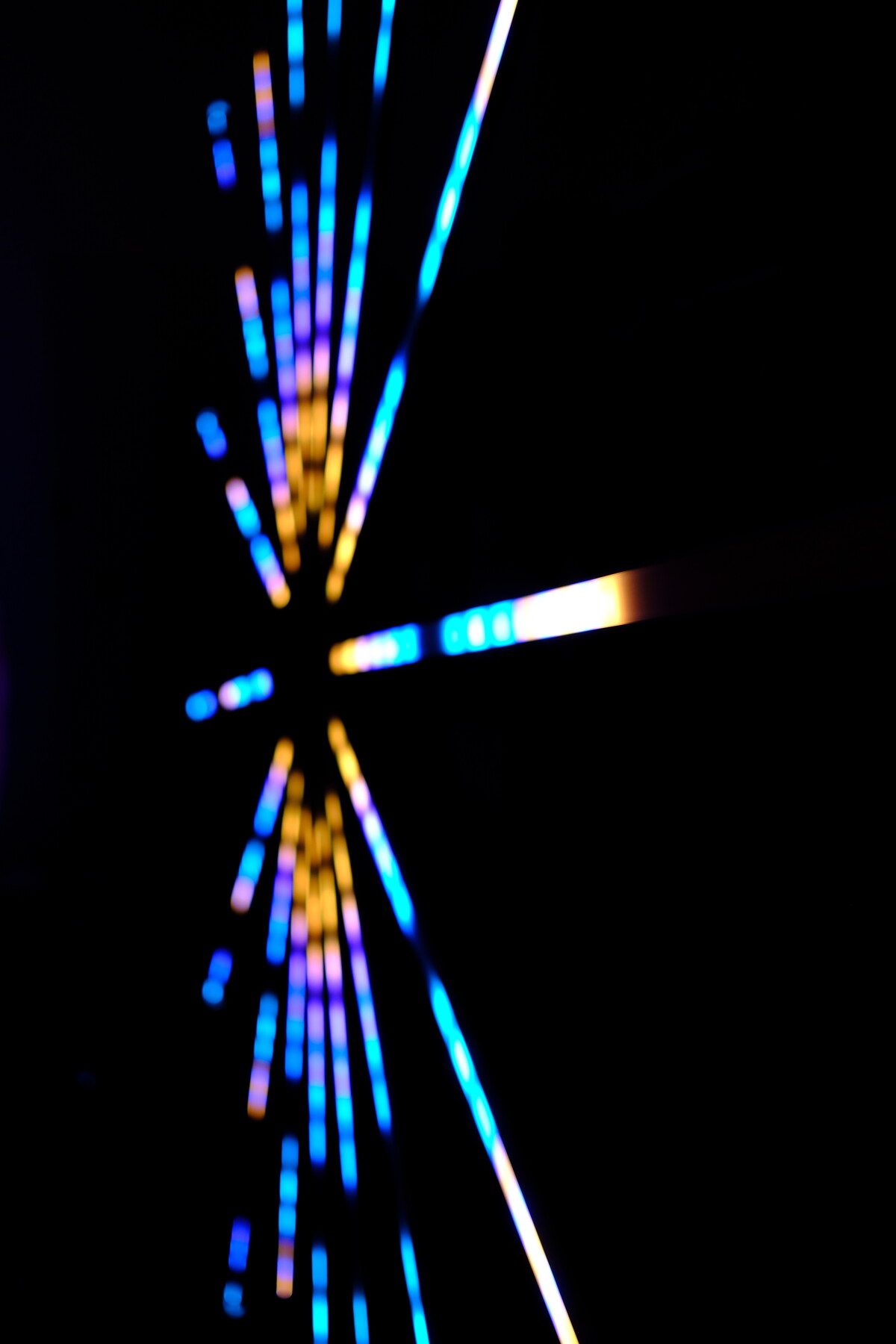 Cyan, purple, and gold LED rays fanning outward from a central point against black &mdash; another angle of Rob&rsquo;s lighting installation.