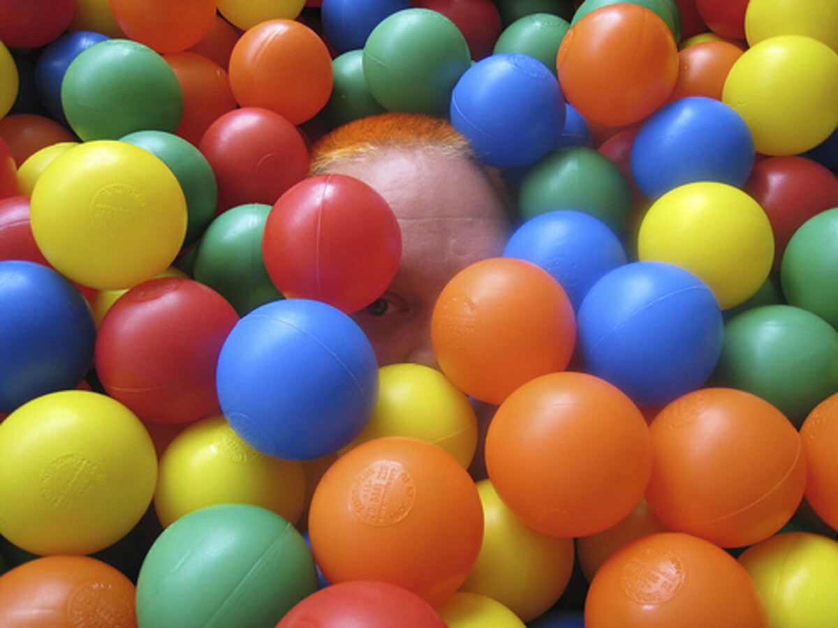 Rob almost completely submerged in a ball pit of red, blue, yellow, green, and orange balls, only his forehead and orange hair patch peeking through.