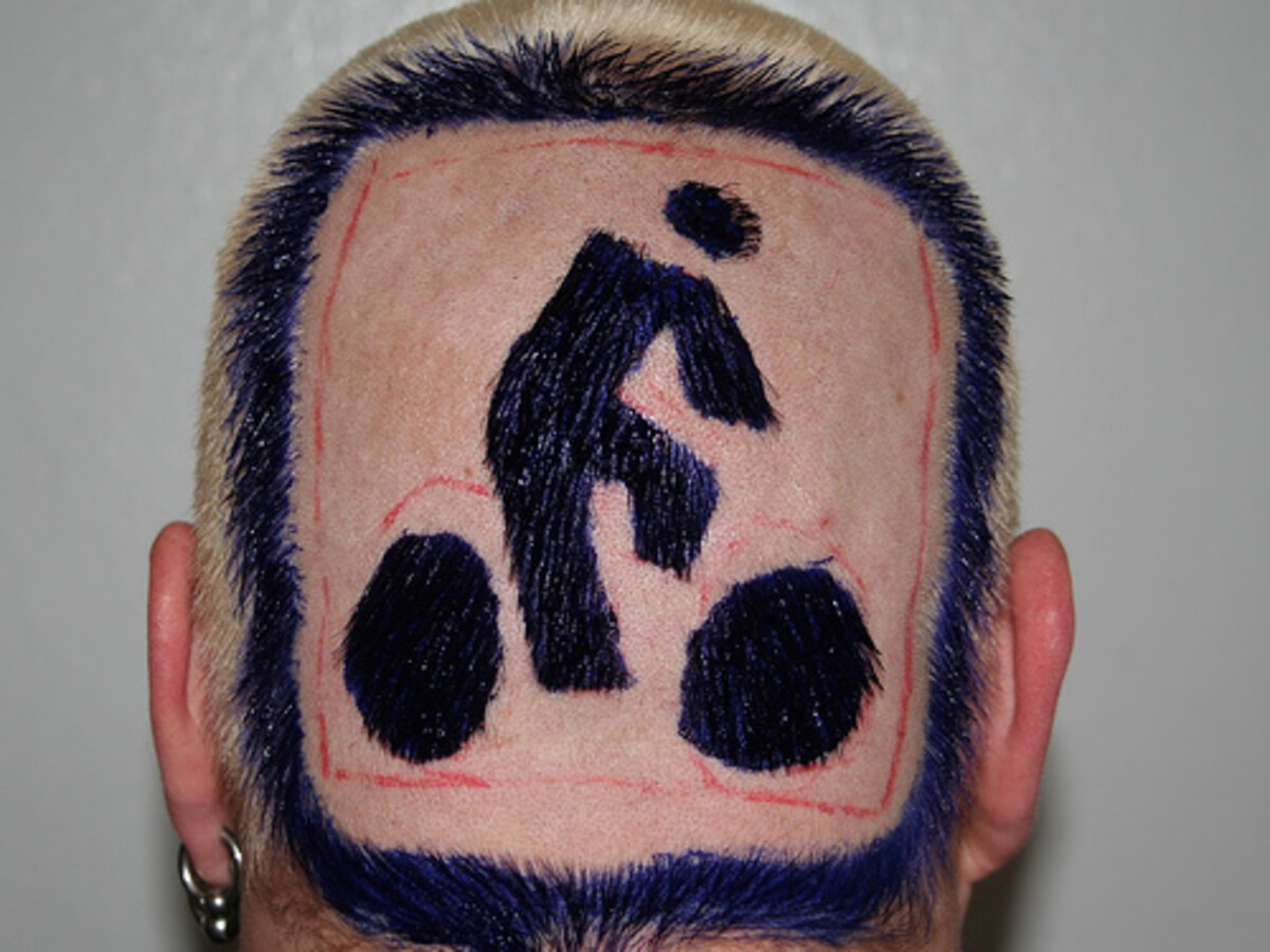 Back of Rob's head showing an intricate shaved design: a dark blue cyclist silhouette inside a red-outlined rectangle, framed by deep purple fringe hair with blonde crown.