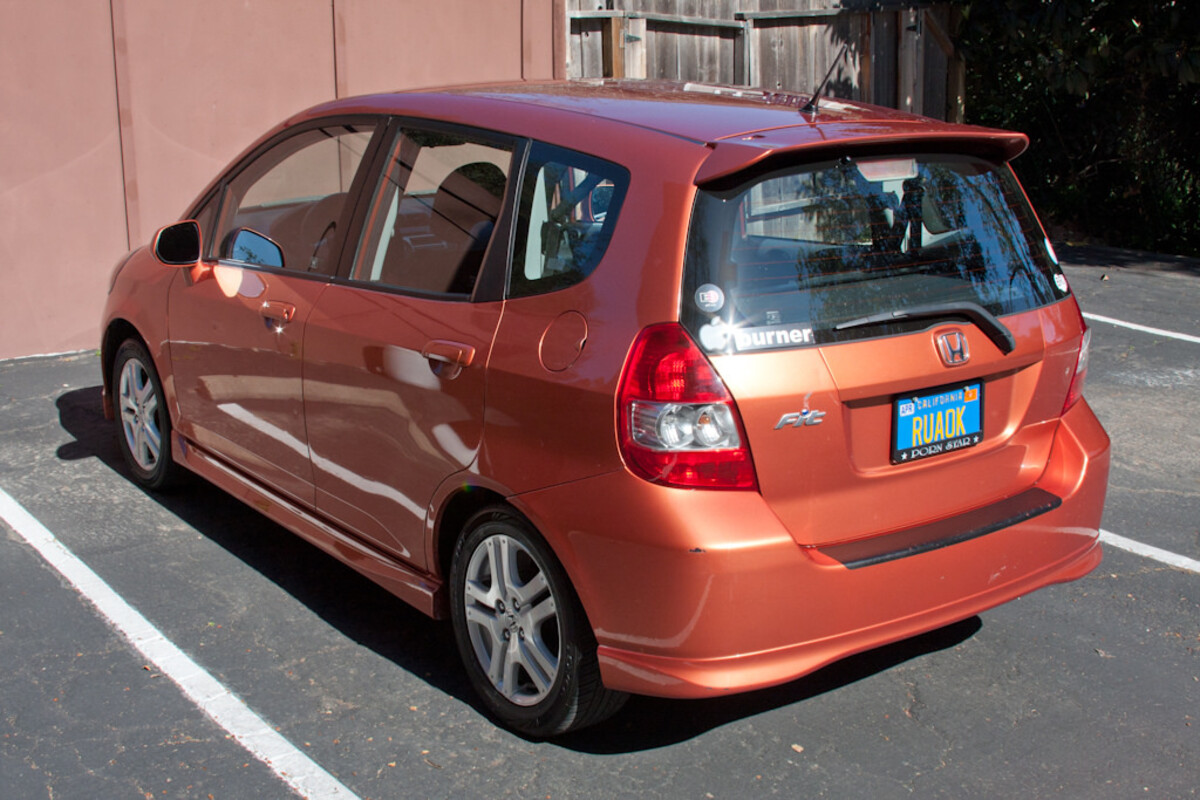 Orange Honda Fit from behind in a parking lot. California license plate reads &lsquo;RUAOK.&rsquo; Window sticker says &lsquo;Burner.&rsquo;