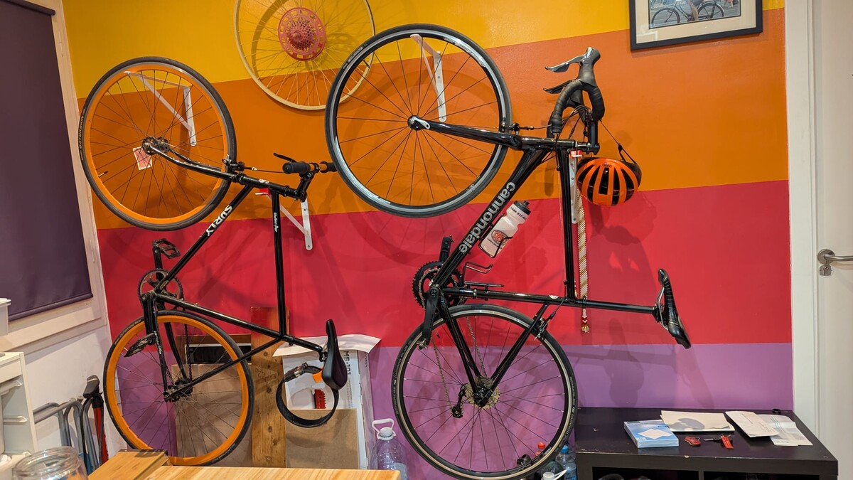 Two bicycles mounted vertically on an apartment wall painted in bold horizontal stripes of orange, yellow, red, and purple, a bicycle wheel hung separately as decoration above.