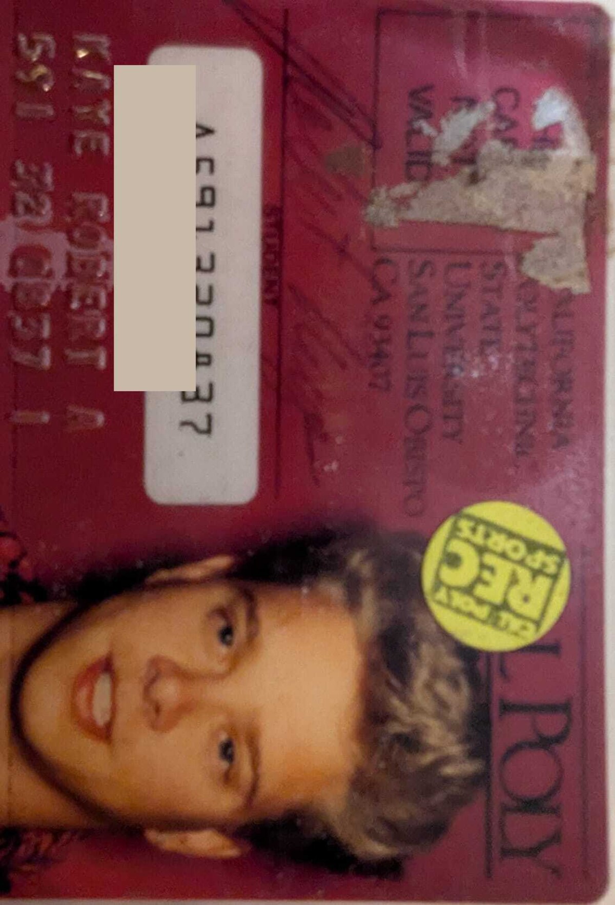 Cal Poly San Luis Obispo student ID card, oriented upside down. Young man with natural blond hair looks up at the camera. A Poly Rec Sports sticker is affixed to the card. Student number redacted.