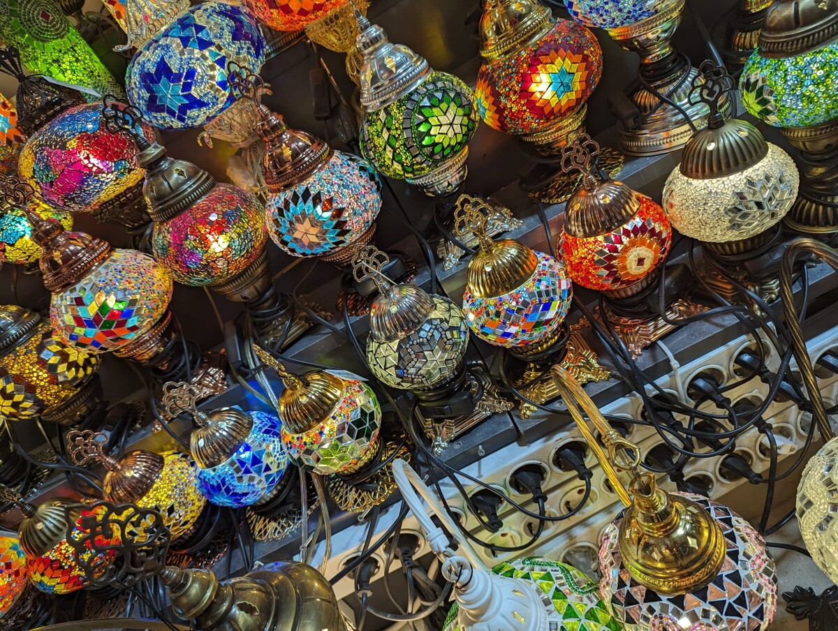 Dense overhead shot of dozens of traditional Turkish mosaic glass lamps hanging in rows, every color represented — reds, blues, greens, golds, purples — with intricate metal filigree frames.