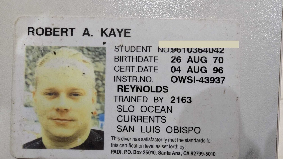 Reverse side of a PADI certification card showing a young man with short blond hair in a small ID photo. Printed details: Robert A. Kaye, birthdate 26 Aug 70, certification date 04 Aug 96, instructor Reynolds, SLO Ocean Currents, San Luis Obispo. Student number redacted.