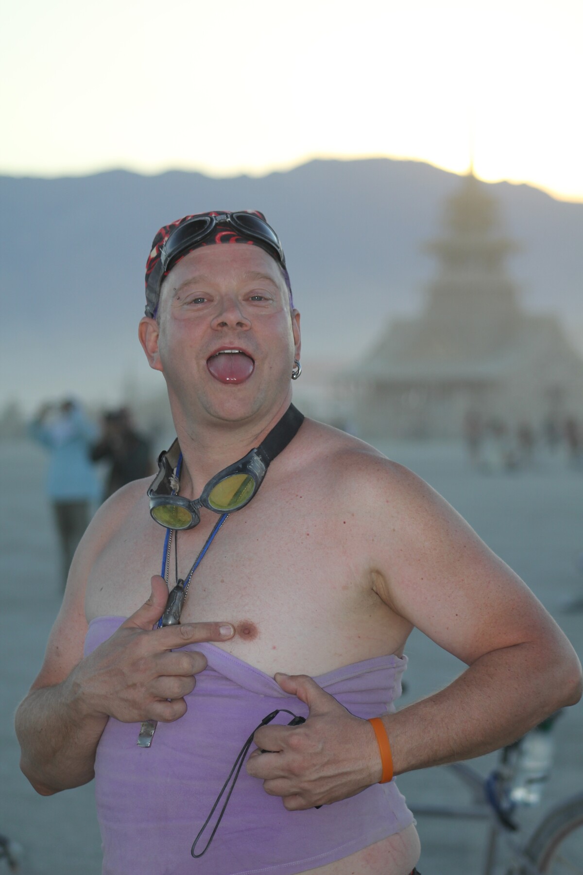 Rob in full Burning Man mode — tongue out, pulling down a lavender tube top, bandana cap, double goggles, hamming for the camera on the playa