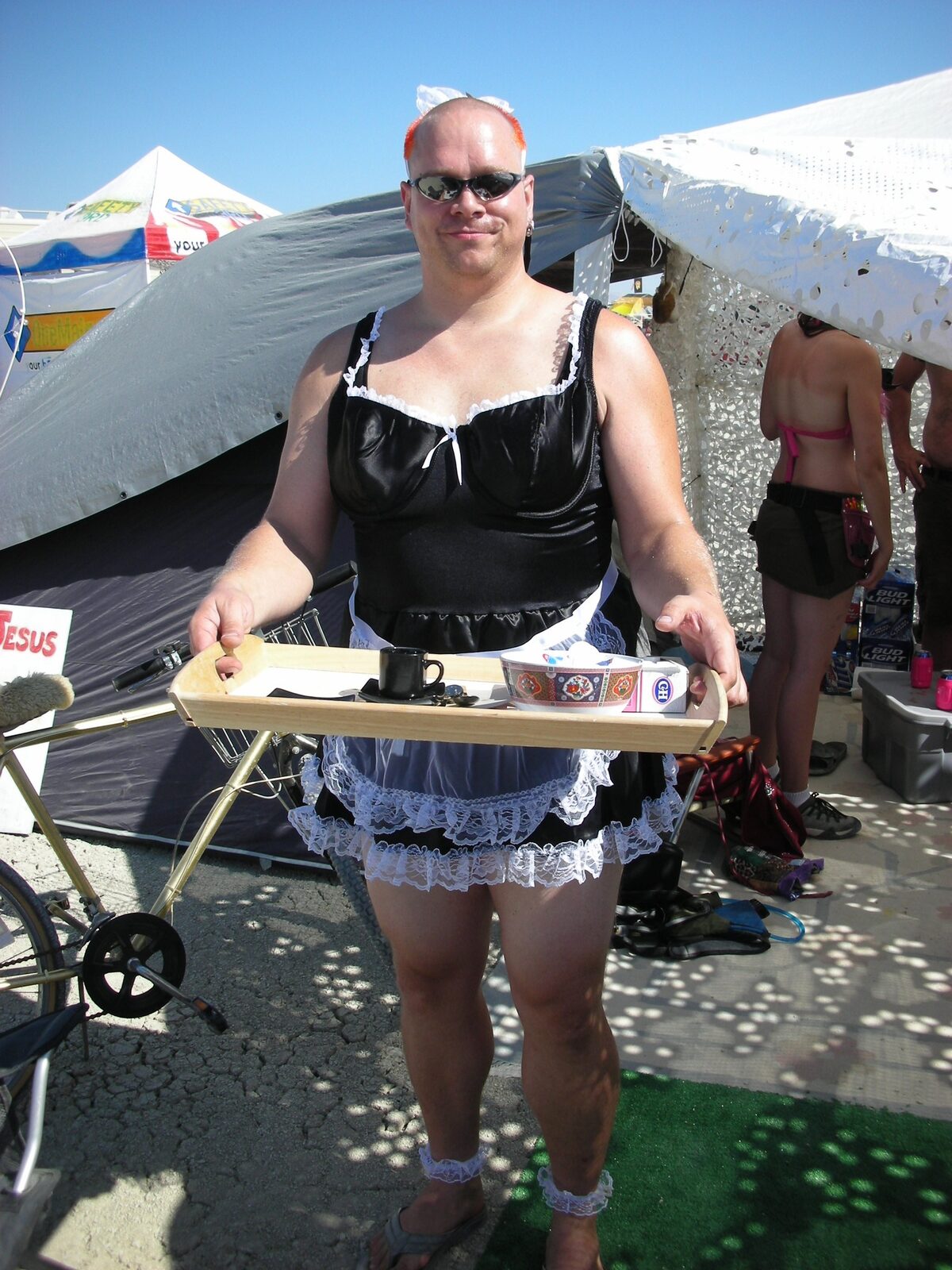 Rob in a French maid outfit at Burning Man, serving tray with coffee, pink mohawk, desert setting